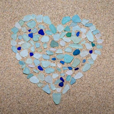 Beautiful blue and aqua blue seaglass forming a heart on a sand background