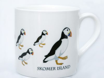 a bone china mug with a graphic art design of multiple puffins on it and the words skomer island