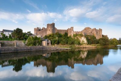 still waters reflecting the blue skies and light clouds with pembroke castle as the main feature