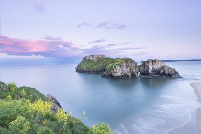 looking towards st catherines island with pale pink clouds and a purple glow surrounding it at high tide in tenby