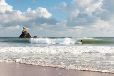 broad haven south beach in pembrokeshire with a beautiful wave in front of church rock and a surfer crouching down in a wave